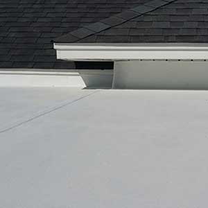 Close up of a residential roof with black shingles but a white, flat roof in front of it